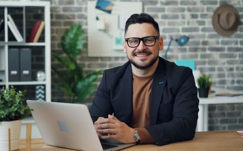 Dueño de una empresa de servicios sonríe frente a su notebook