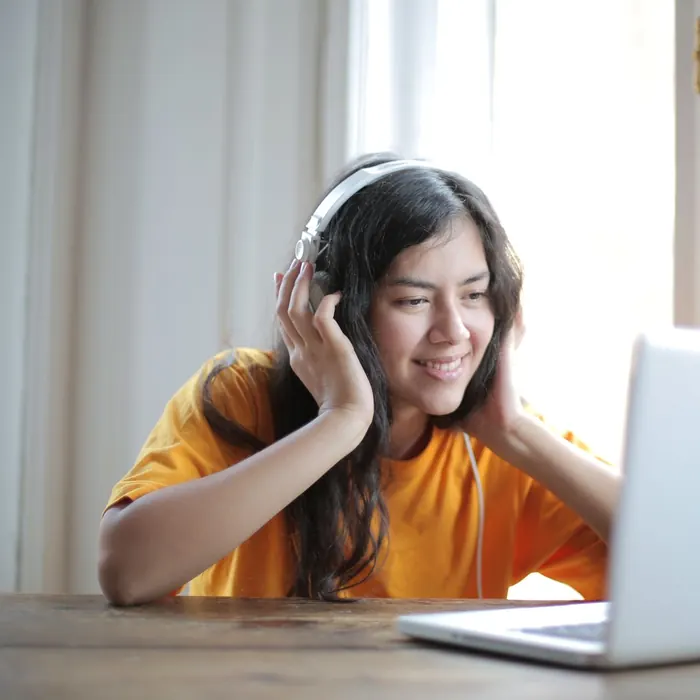 Alumna con audífonos sonríe frente al notebook mientras estudia